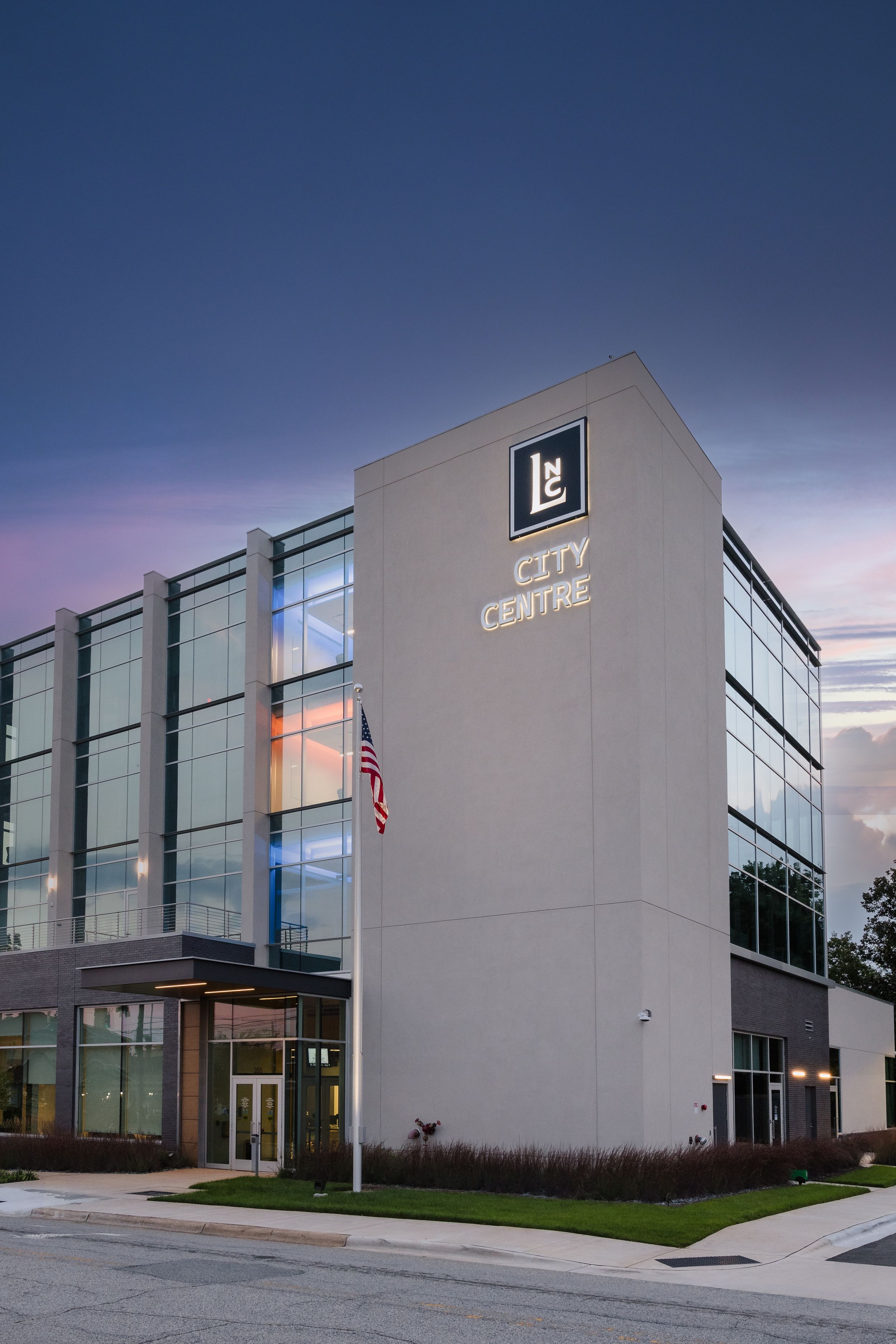 Modern commercial building exterior with glass walls photographed at dusk.