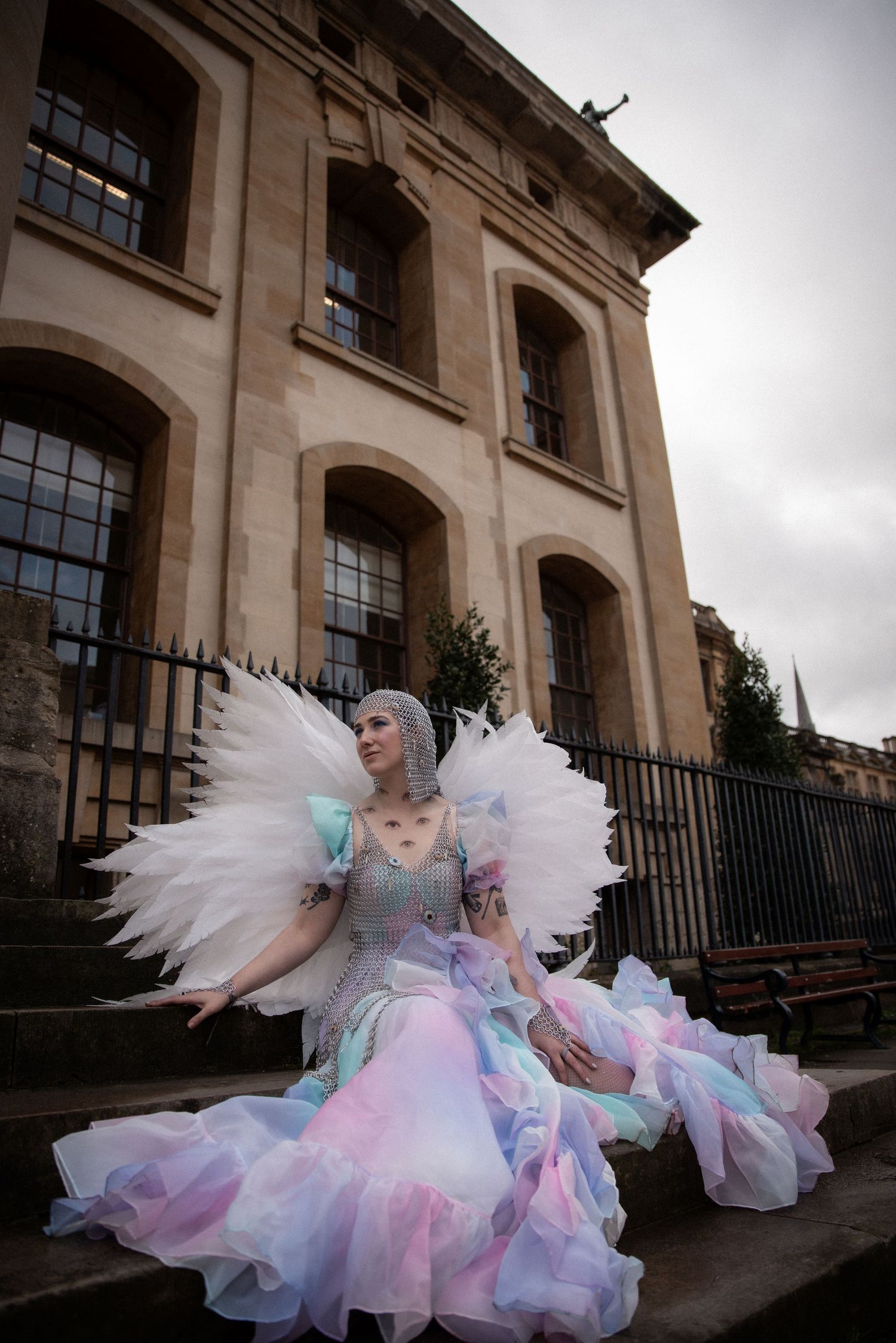 Person in fantasy, ethereal pastel tulle dress poses against stone building facade.