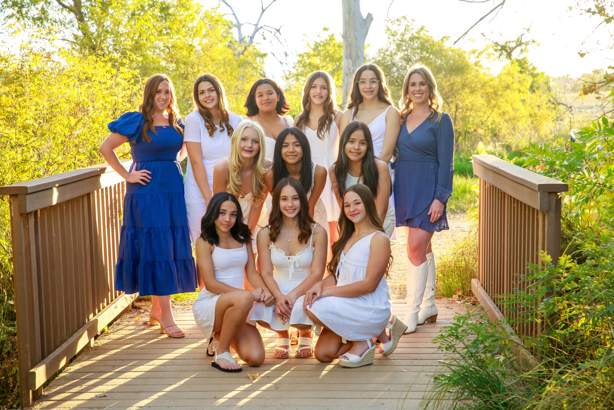 A group sits together on wooden steps surrounded by lush green foliage on a sunny afternoon.