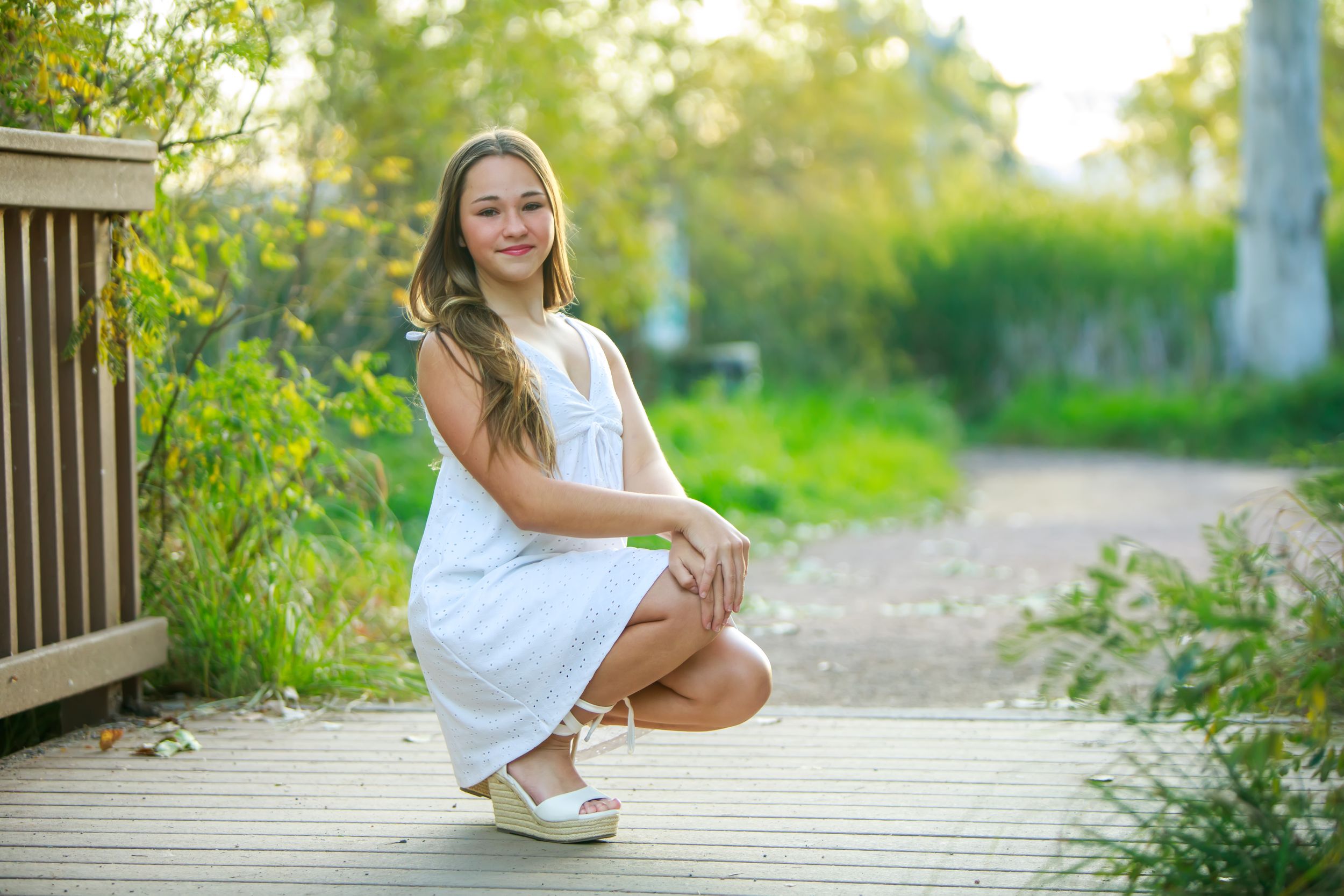 A person in white summer attire sits on wooden steps surrounded by lush greenery in a peaceful outdoor setting.