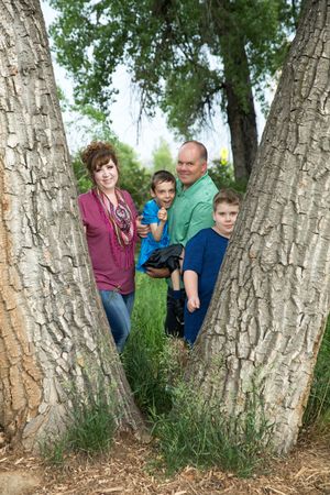 A group stands together between two large tree trunks in a natural outdoor setting on a sunny day.
