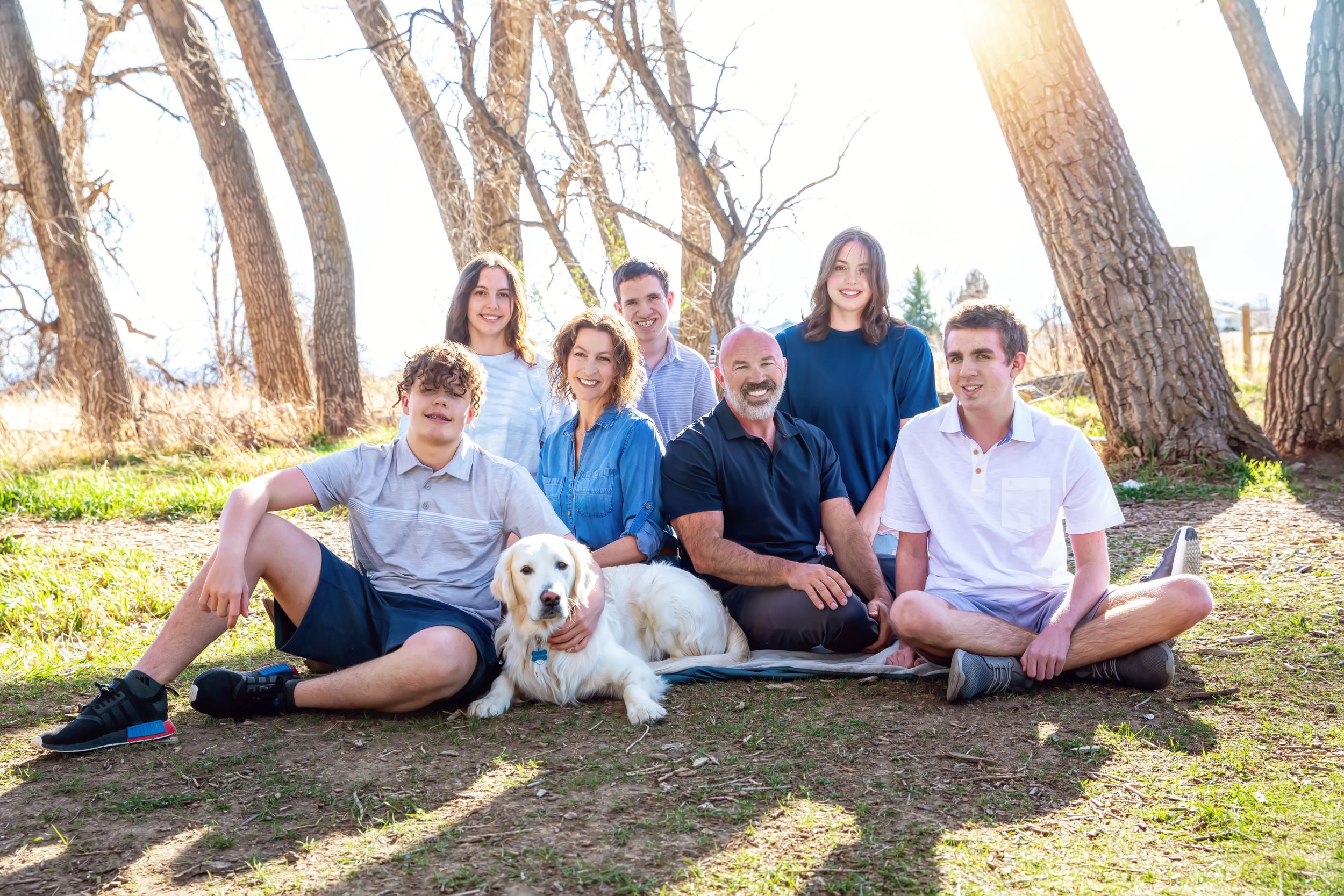 A group sits together under tall pine trees on a grassy slope during golden hour.