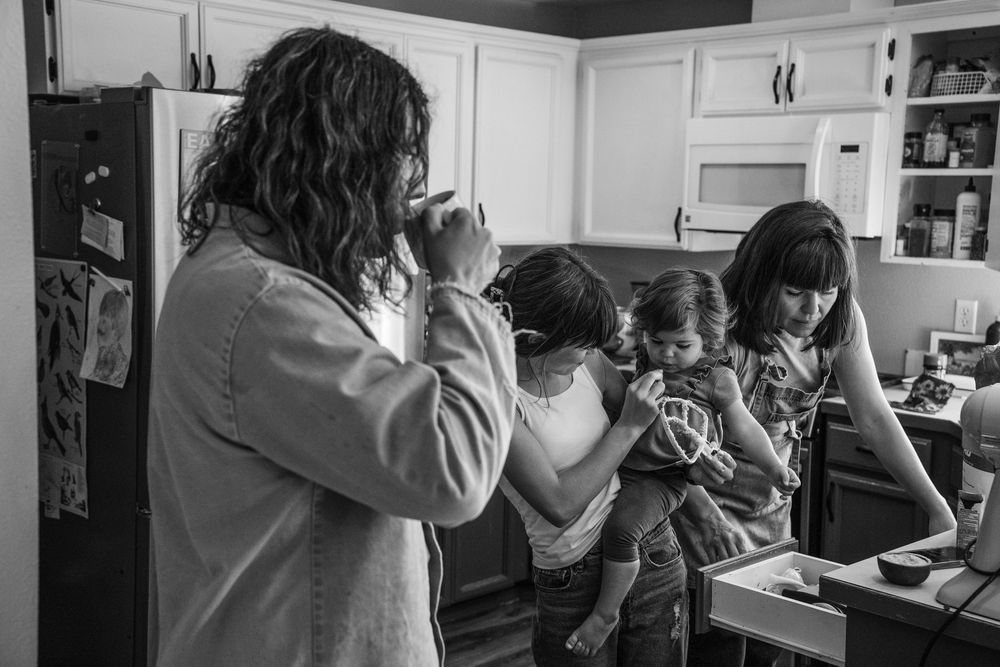 A black and white photo shows people gathered in a kitchen drinking from mugs and cups.
