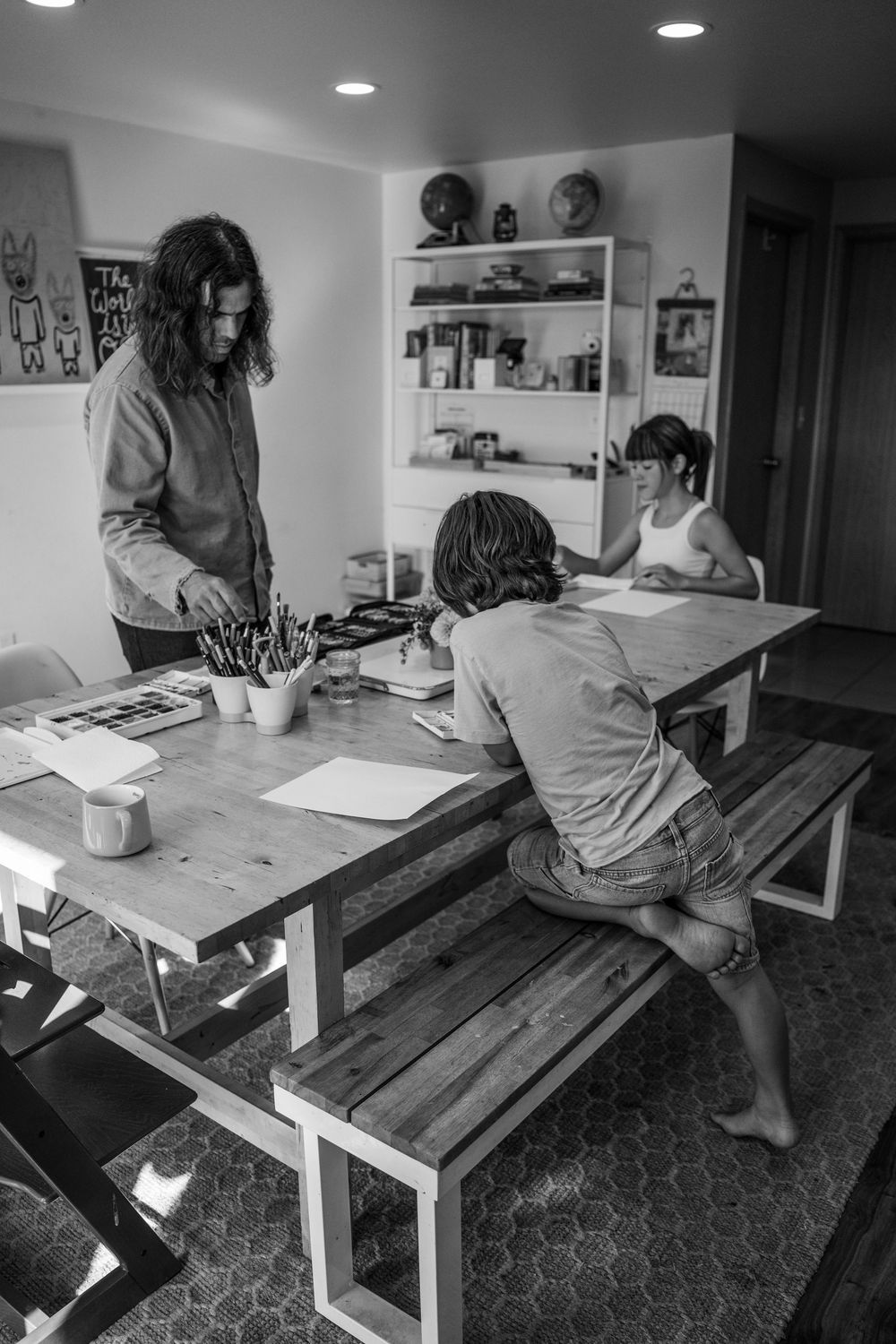 Family working on art or homework together at a wooden table in a home setting.