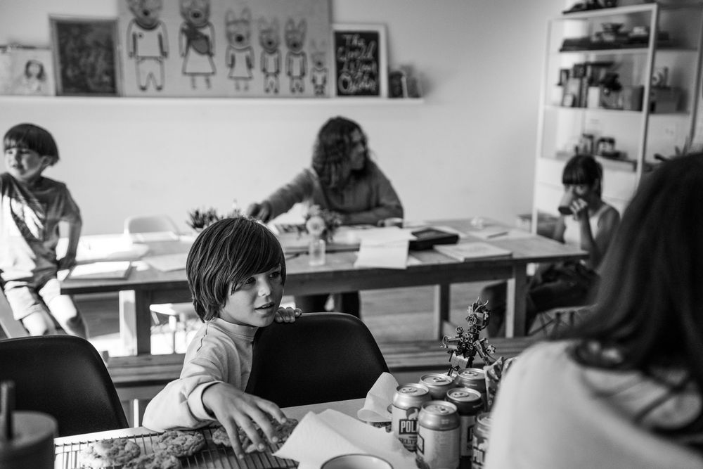 Students work at sewing machines in a black and white classroom setting with art displayed on the walls.