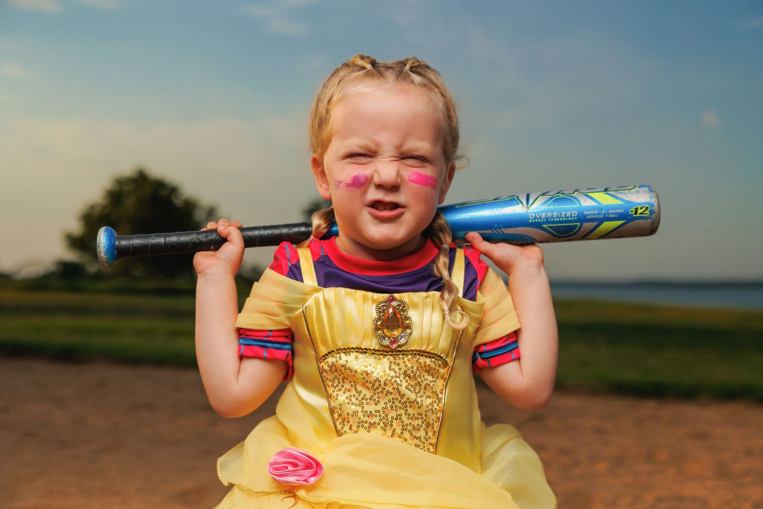 A young baseball player in a yellow uniform holds a bat over their shoulders while standing in a grassy field.