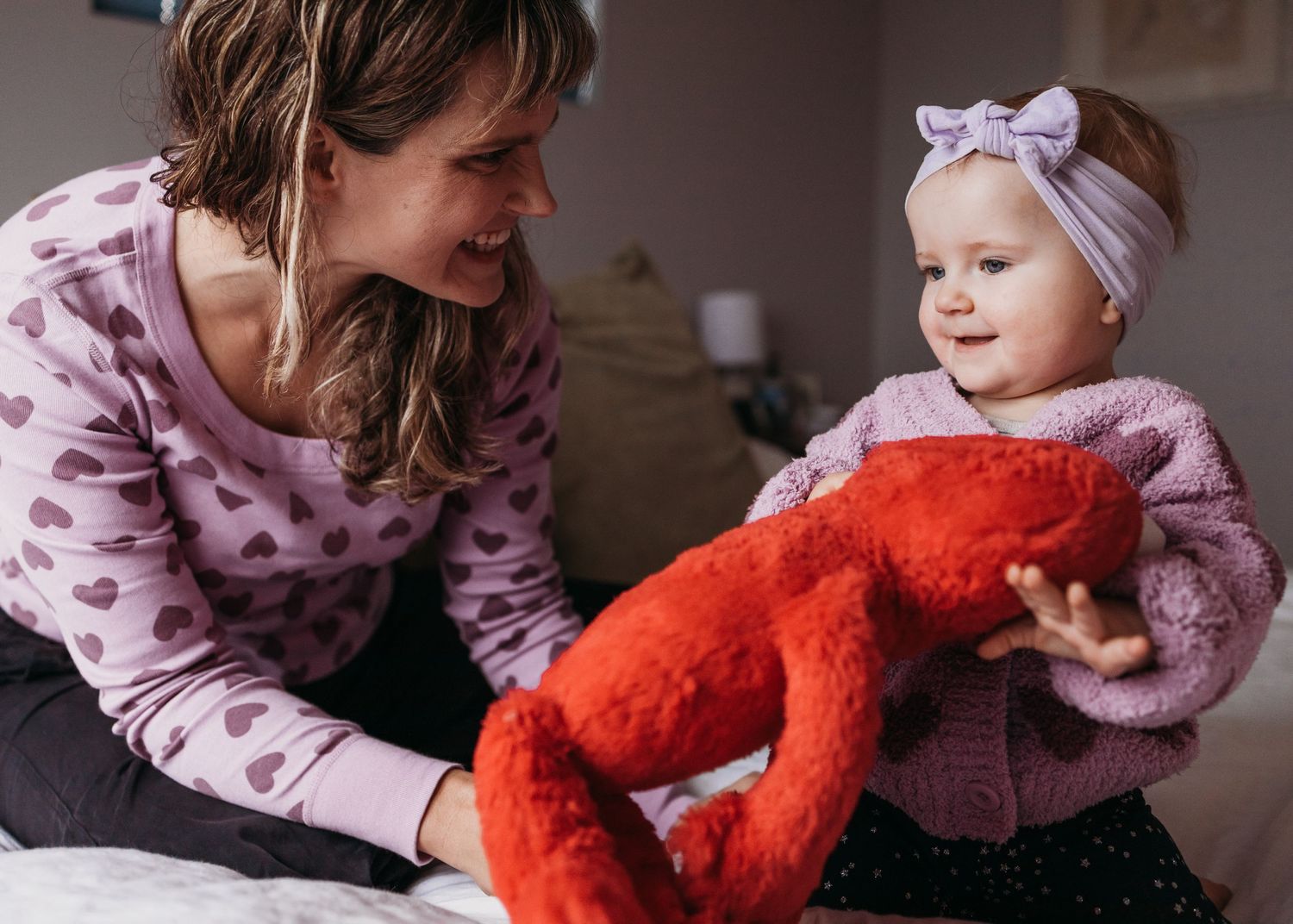 A caregiver and child play together with a bright red plush toy on a dark surface.