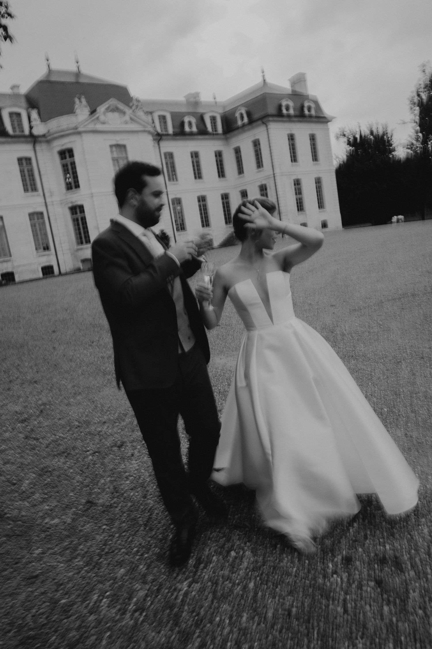 A couple dances playfully on the grounds of a grand French chateau in black and white.