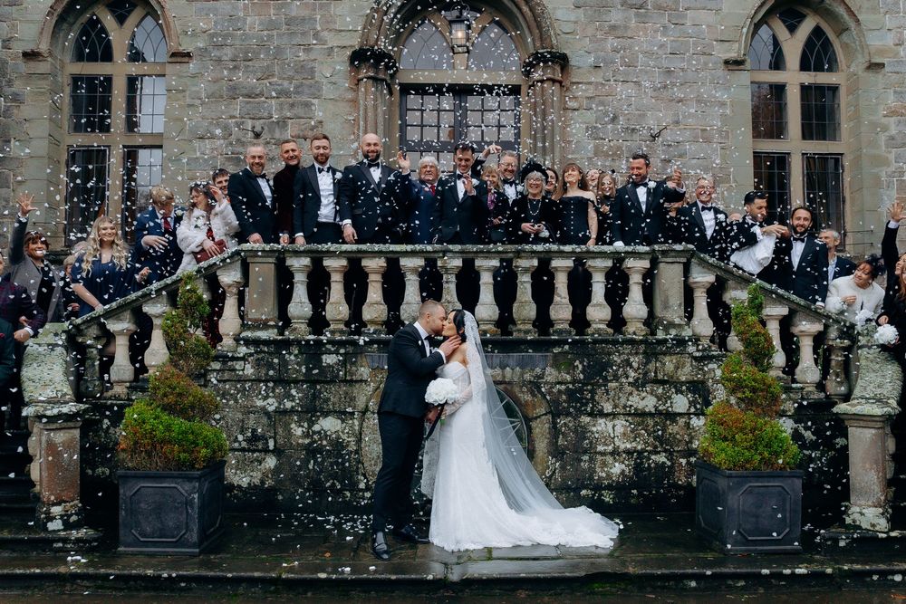 Wedding couple and guests gather on stone steps of historic castle for outdoor ceremony and celebration.