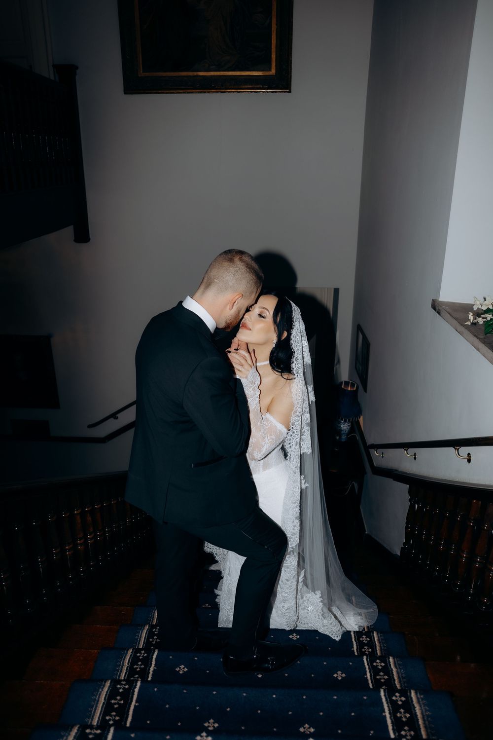 A romantic wedding couple shares an intimate kiss while sitting together in a dimly lit room.