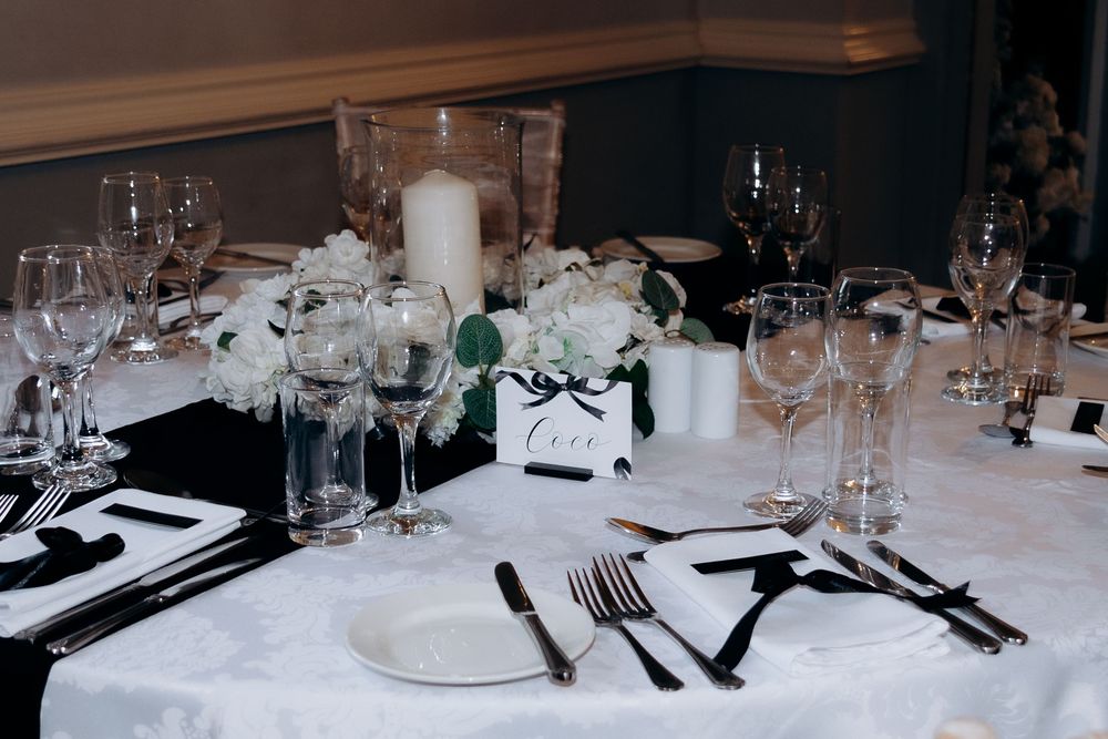 A long formal dining table with white tablecloths, wine glasses, and elegant place settings in a banquet setting.