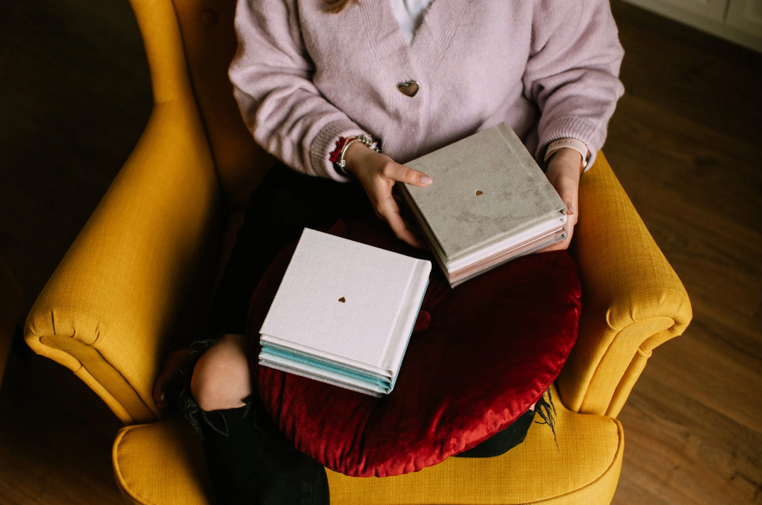 Person sitting in a yellow armchair wearing pink cardigan and holding a book in a cozy reading nook.