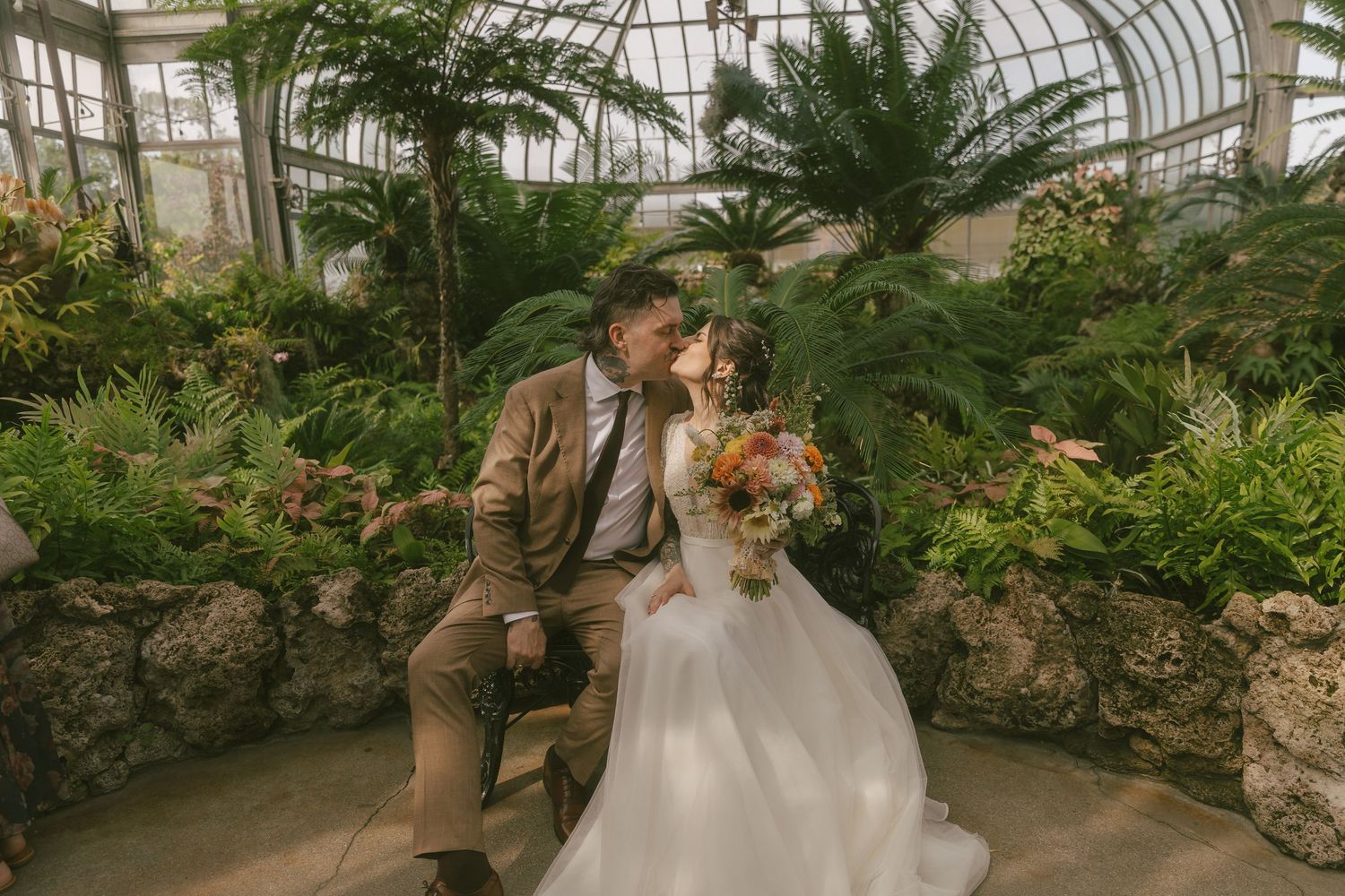 A couple shares romantic moments in a lush greenhouse conservatory during a wedding photo session.