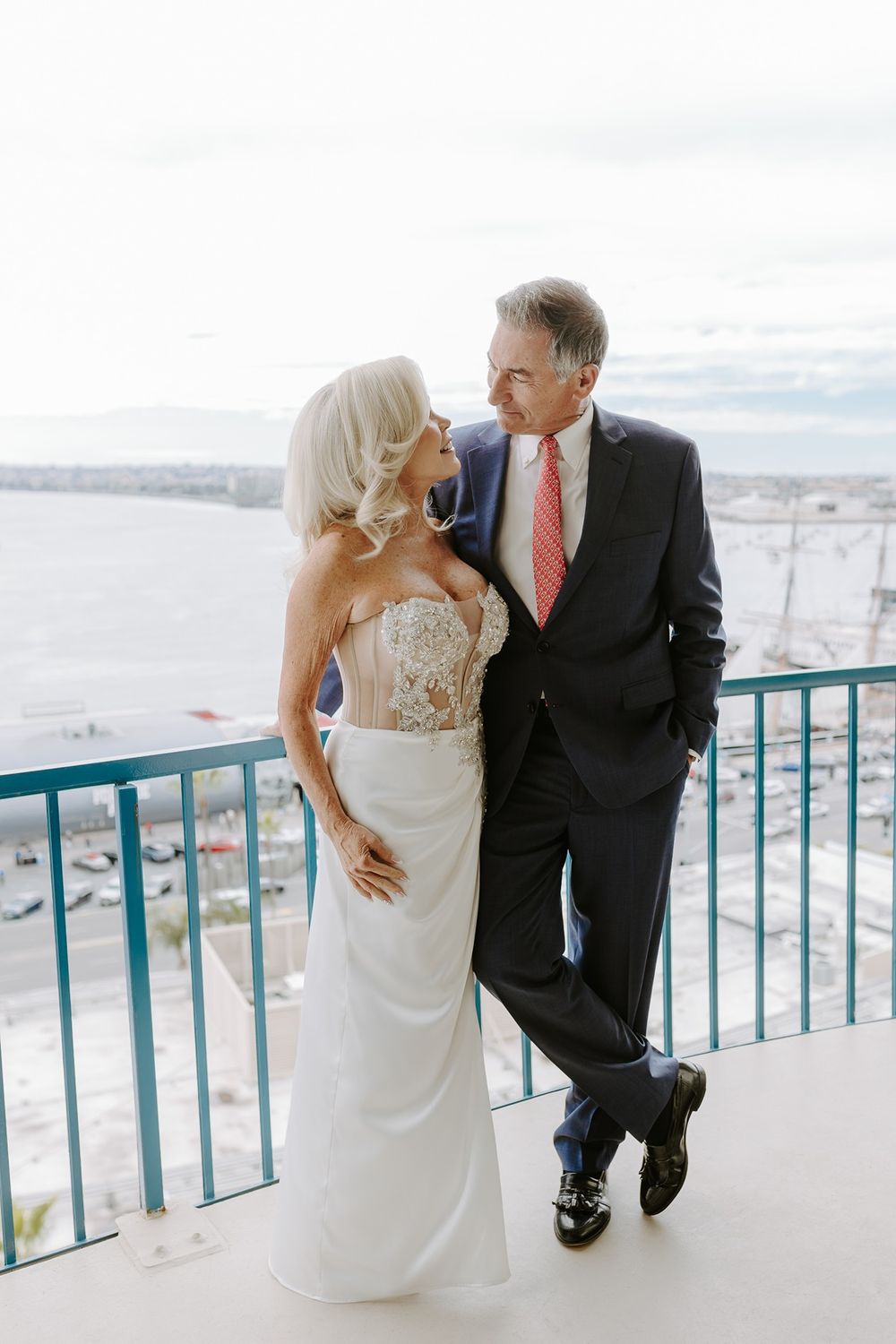 A couple in wedding attire share intimate moments on an oceanfront balcony with turquoise railings.