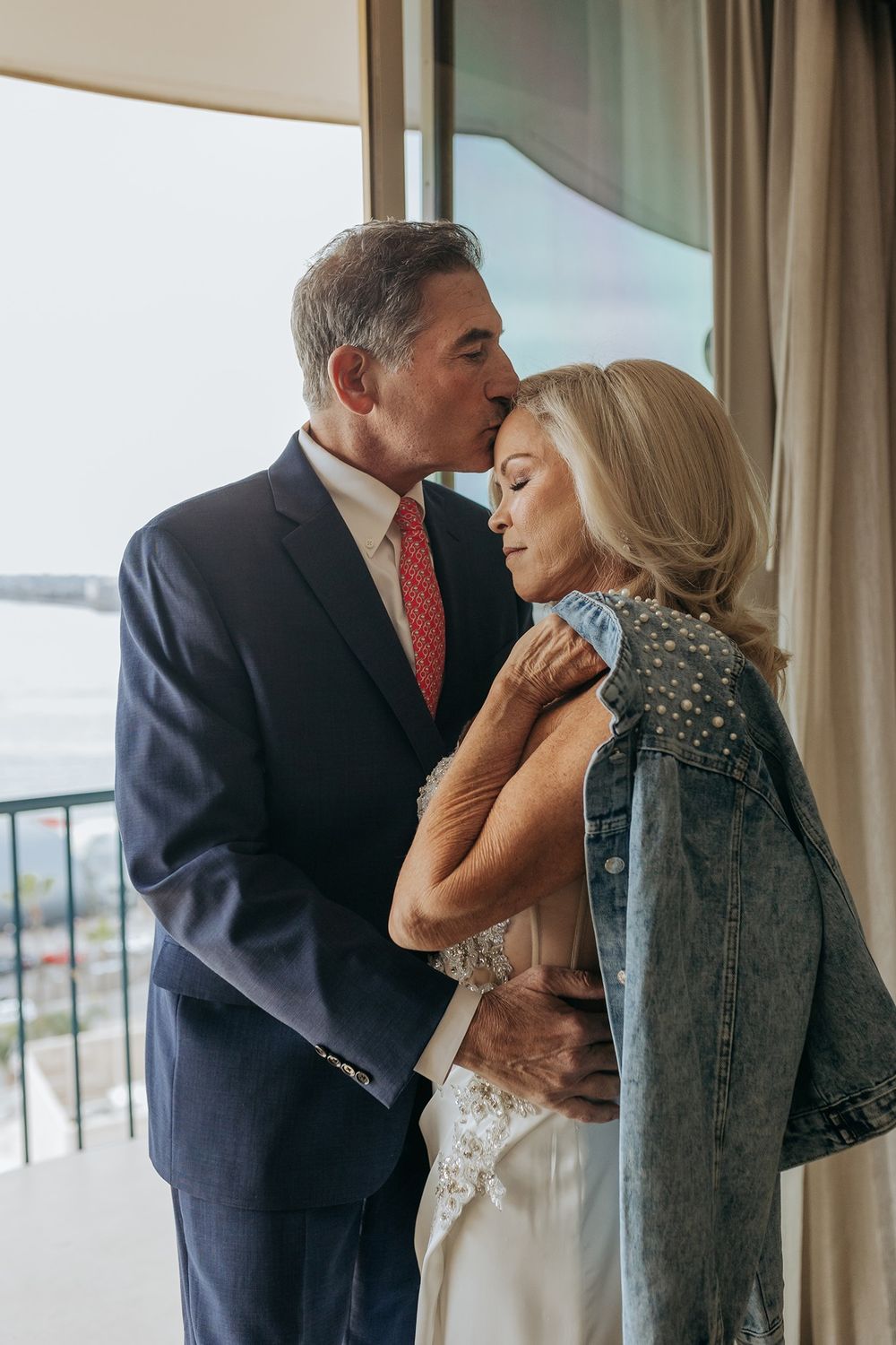 A series of tender moments between a bride and groom during a wedding day by large windows.