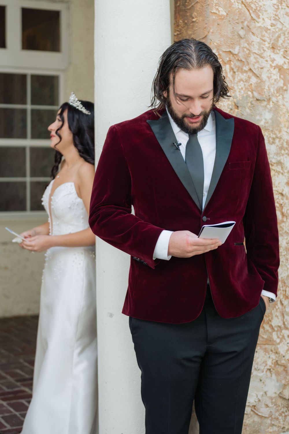 Wedding photos showing someone in a burgundy velvet tuxedo jacket reading a letter beside elegant columns.