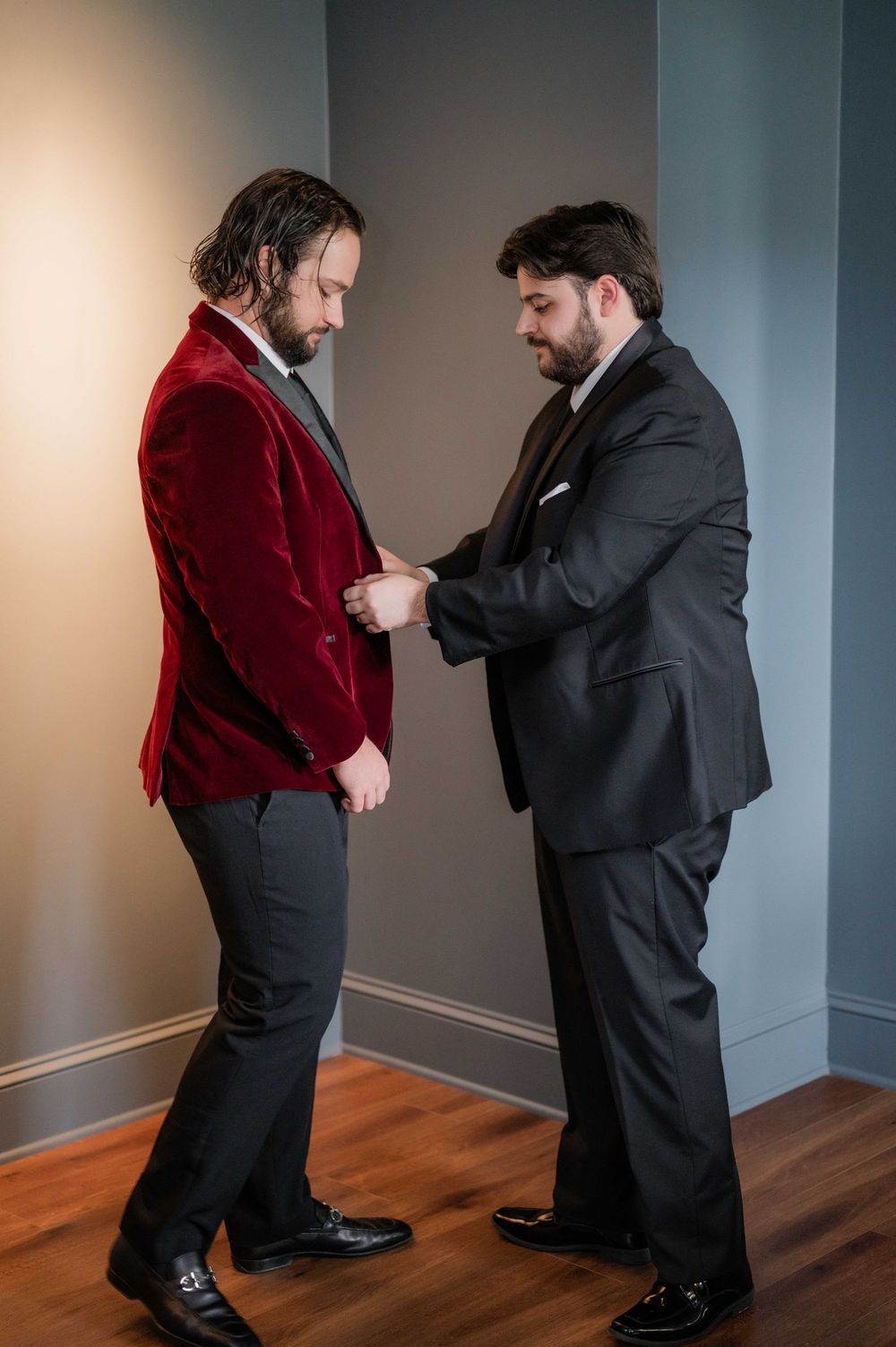 Two people in formal attire dance together in a room with gray walls and hardwood floors.