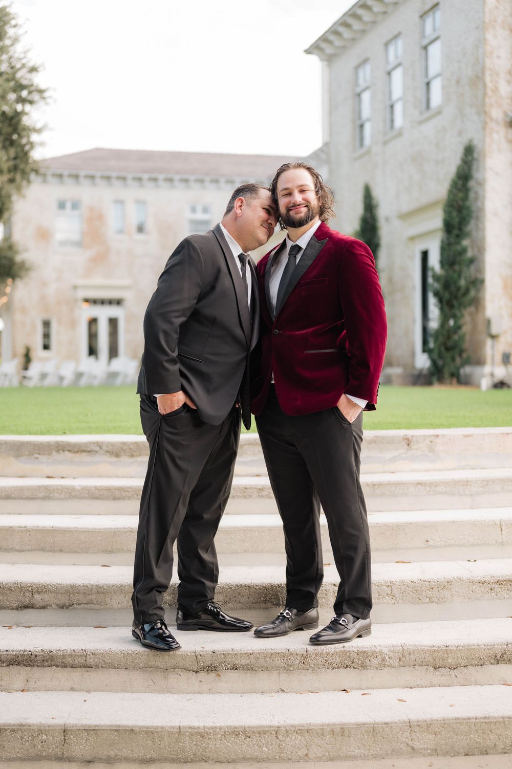 Two people in formal attire sit together on stone steps in front of a building.