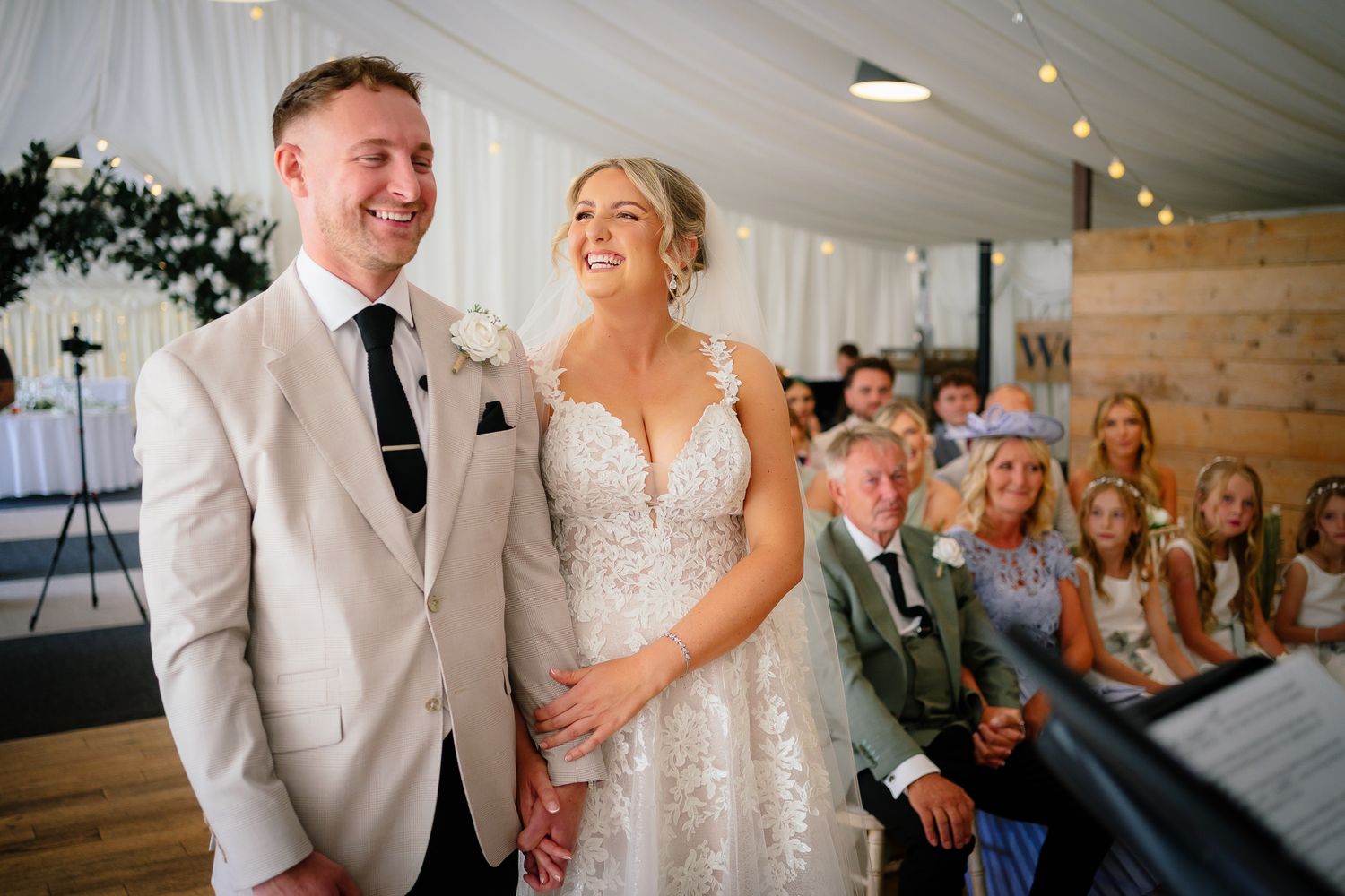 A joyful wedding celebration inside a white tent reception venue with guests seated at tables.