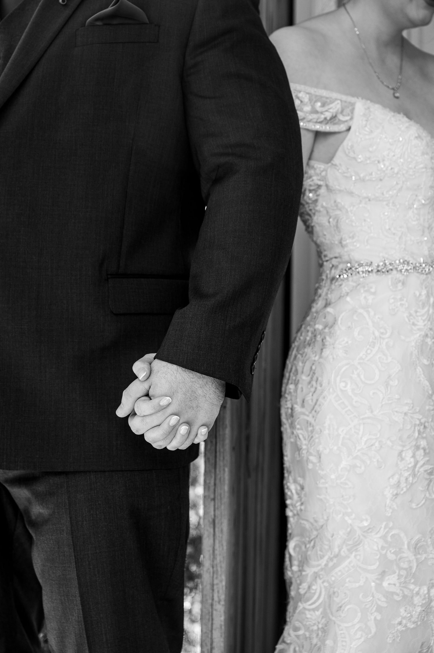Close-up black and white shot of couple holding hands in wedding attire.