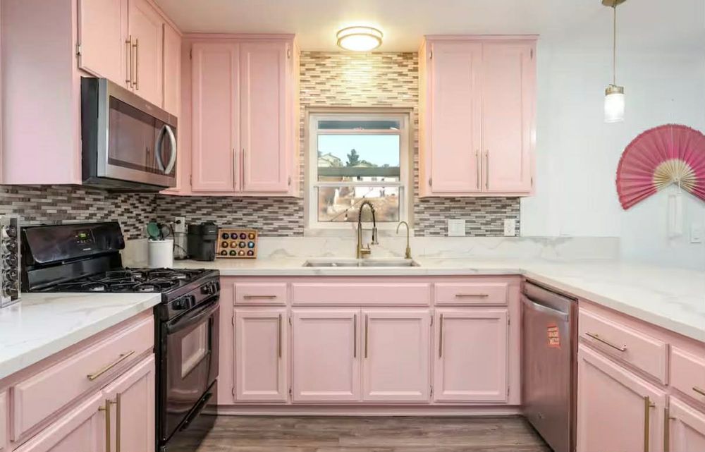 Modern kitchen interior with pink cabinets, pendant lights, and mosaic tile backsplash features a clean, contemporary design.
