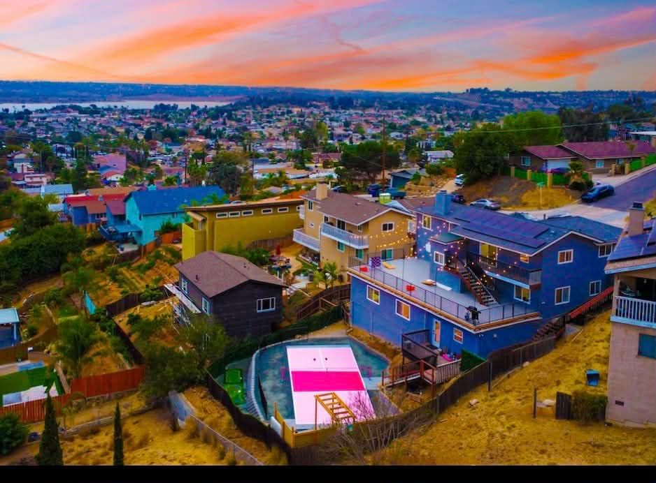Panoramic aerial view of coastal houses and buildings under a vibrant orange and pink sunset sky.