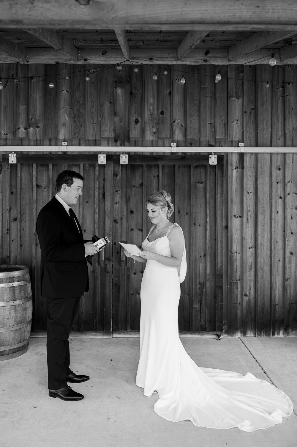 Wedding couple exchanges vows in front of rustic wooden wall with vintage barrel decor.