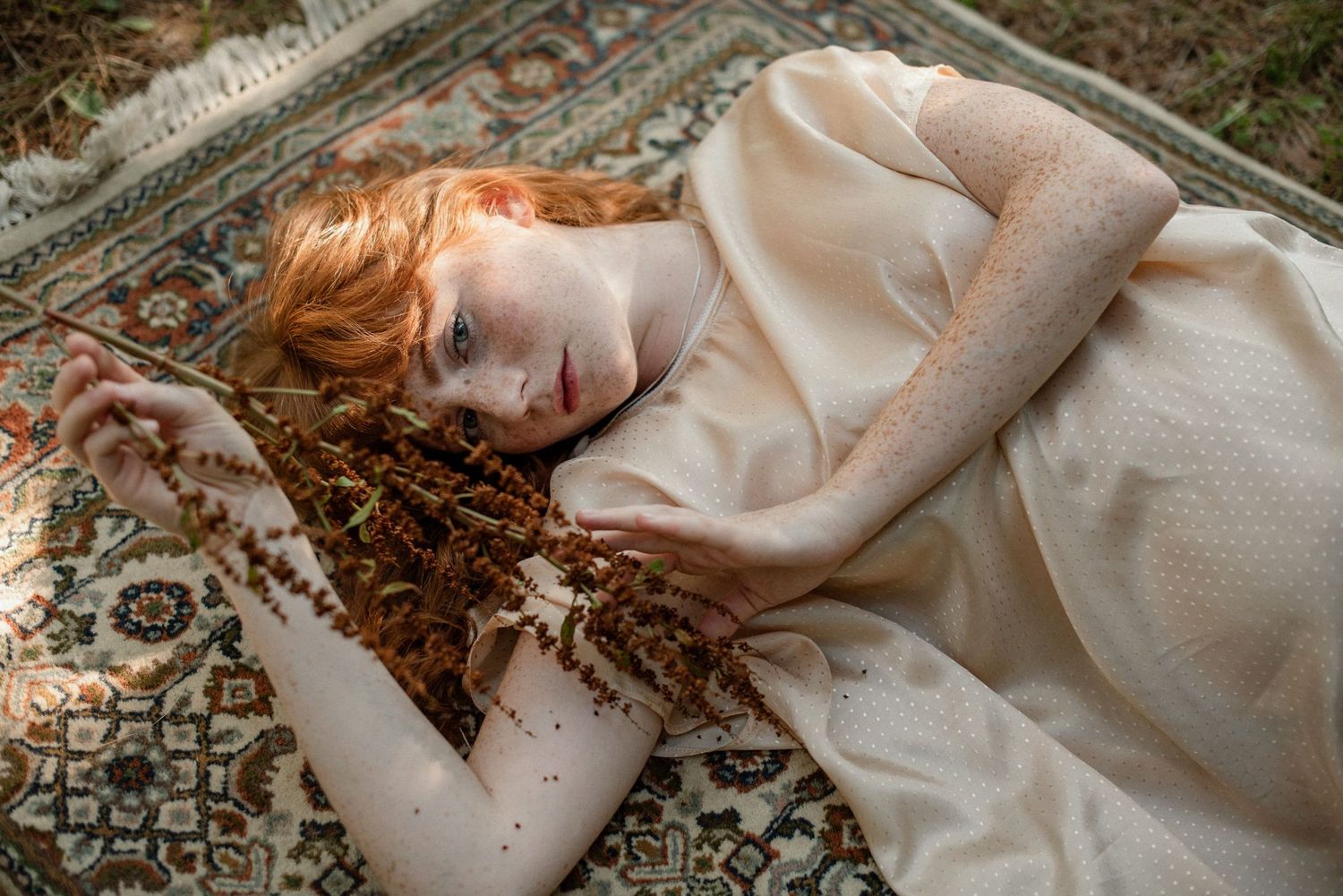 Portrait of a red-haired woman lying on a patterned rug, photographed in soft natural light by photographer Yanique Fillion.