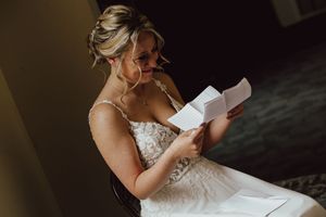 A bride in a white lace gown adjusts her dress while getting ready for her wedding ceremony.
