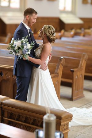 A romantic wedding moment captured in a church pew with elegant white flowers and navy suit details.