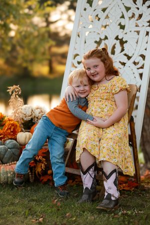 Two children in casual attire sit together on a white garden bench during a golden autumn sunset.