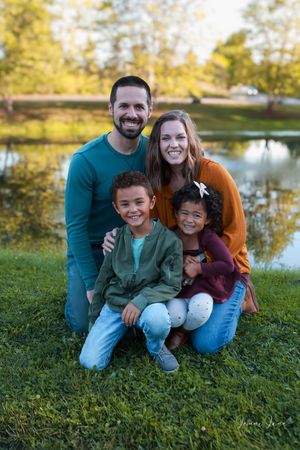 A family sits together on green grass near a tranquil pond during a sunny autumn day.