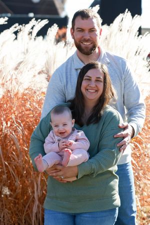 A happy family poses together outdoors against tall ornamental grasses on a sunny autumn day.