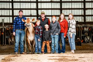A group of people stand in a line showing their jeans and boots against a barn wall background.