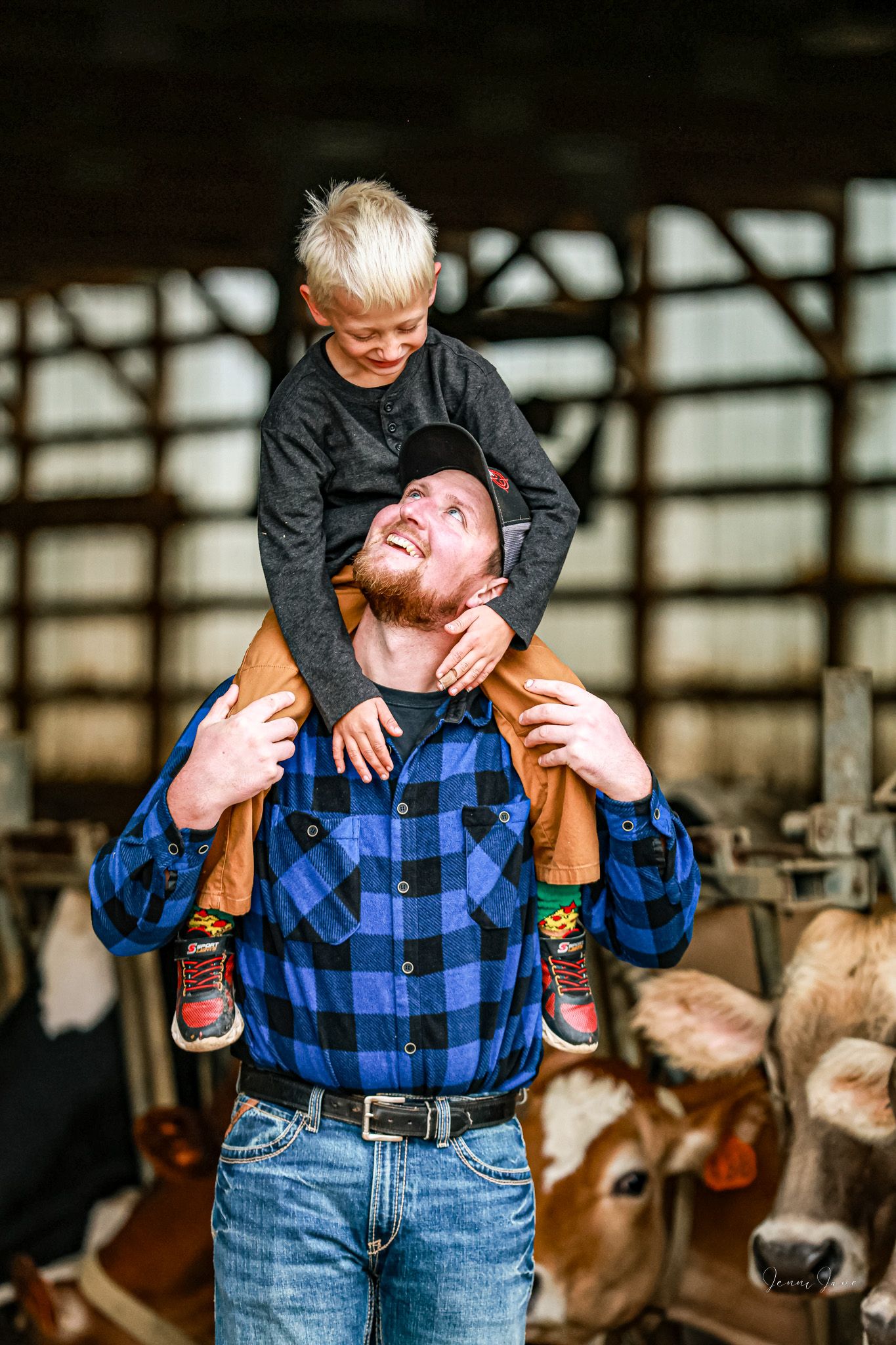 A playful moment captured in a barn as someone lifts a small child while wearing a blue plaid shirt.