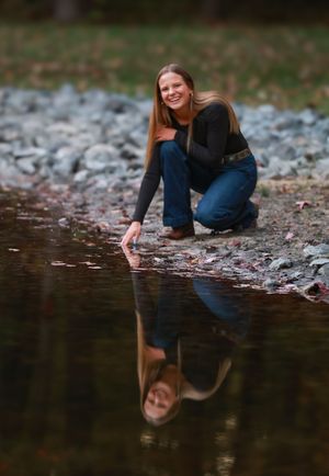 Person in blue denim kneeling by reflective water's edge in autumn setting creating artistic reflection photo.