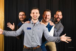A group of people in casual business attire smile and pose together against a dark background.
