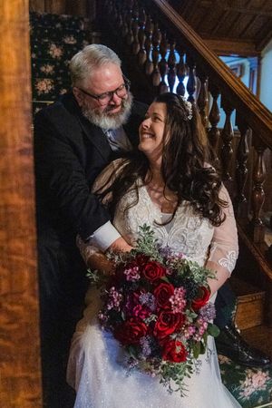Couple shares a joyful moment at their wedding ceremony with a stunning burgundy and red rose bouquet.