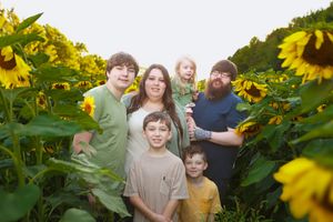 A group poses together in a vibrant sunflower field on a sunny day, surrounded by tall yellow blooms.