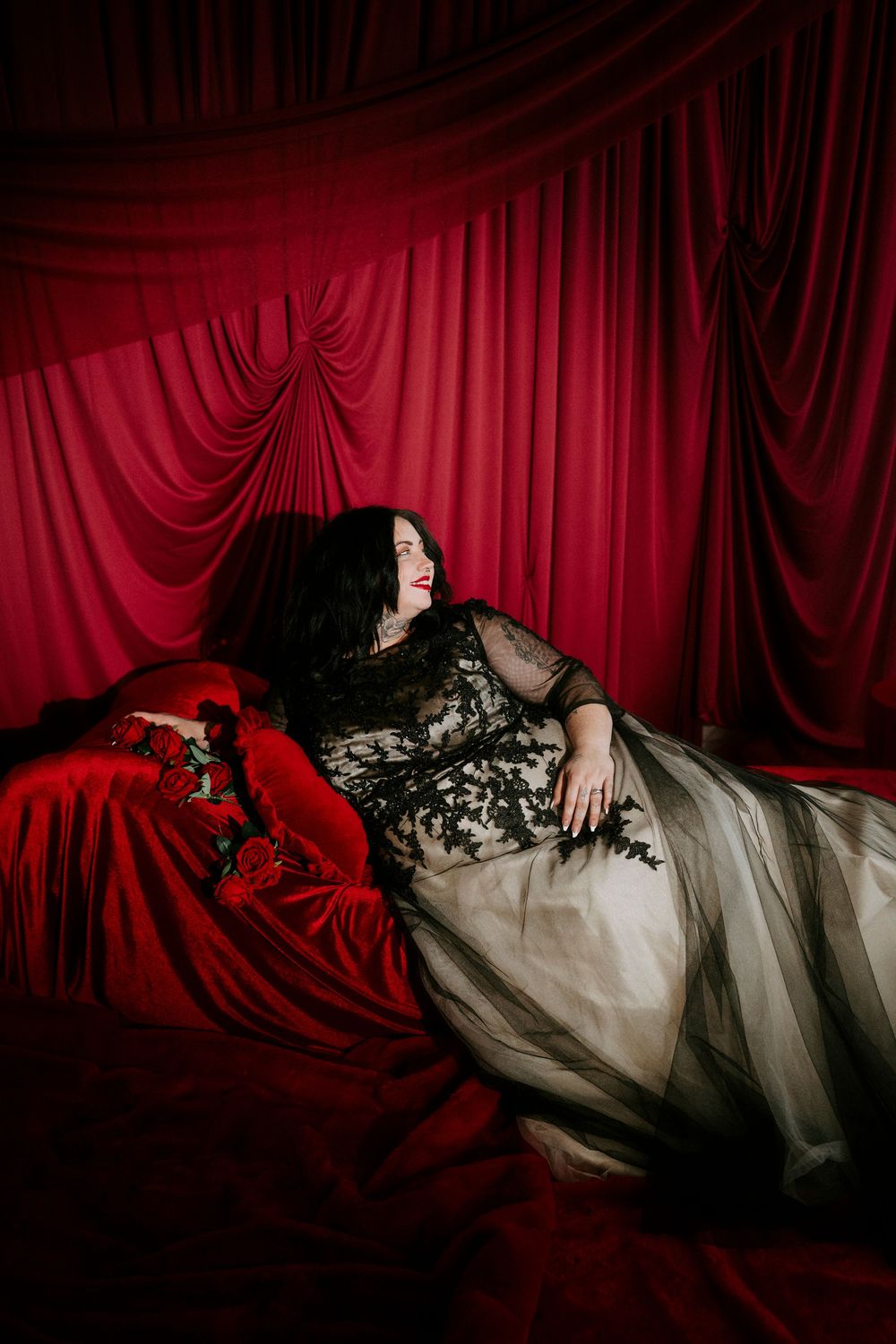 Dramatic portrait series against red velvet curtains featuring a figure in black lace and white fabric in reclining poses.