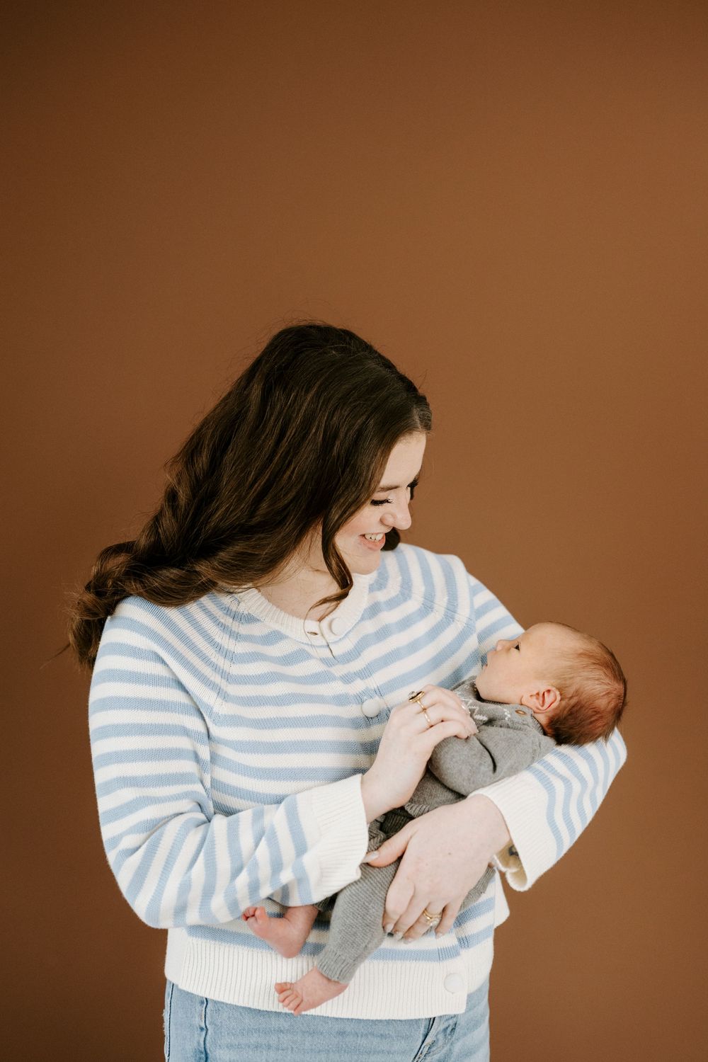 A tender moment between parent and newborn baby in a striped sweater against a brown backdrop.