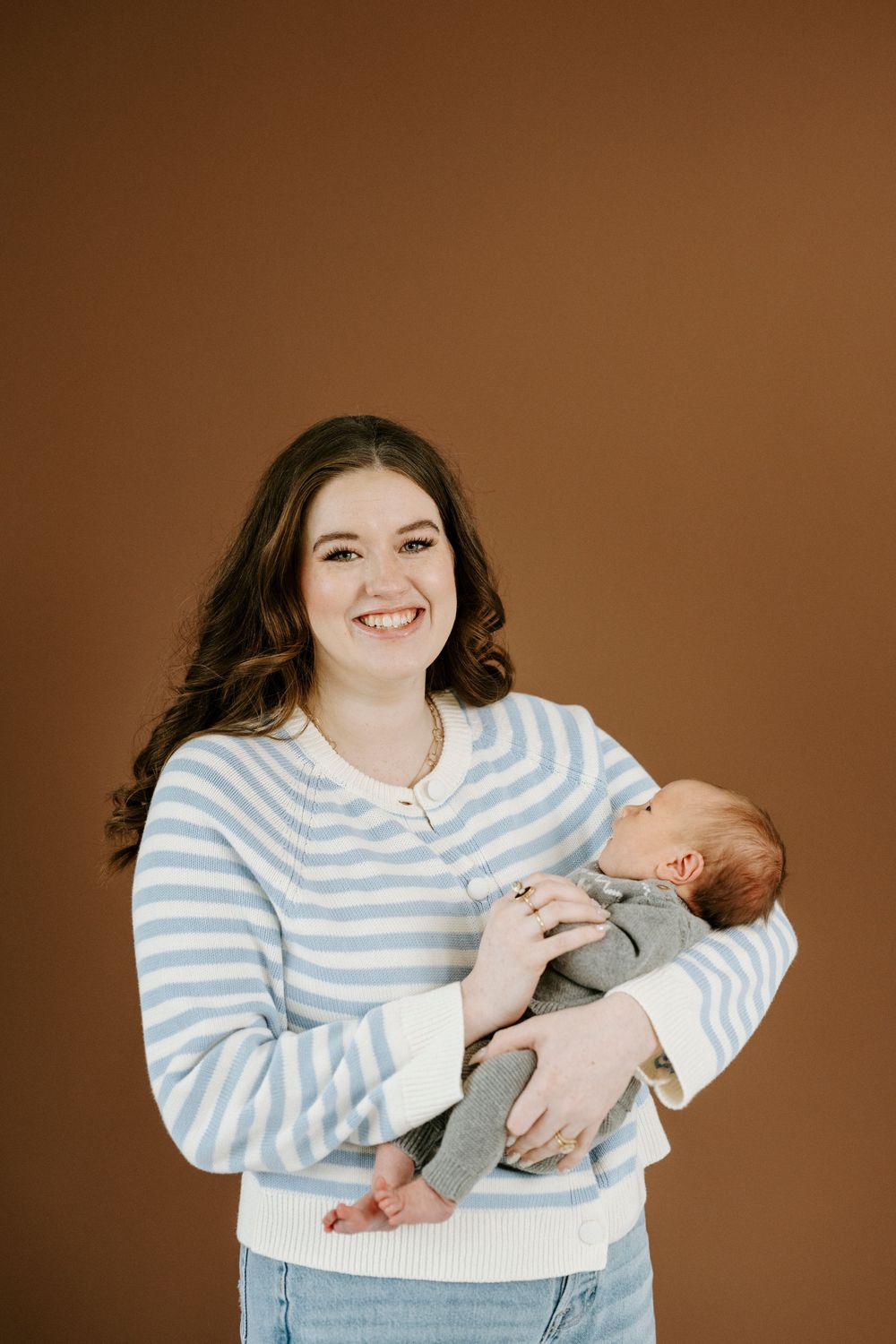 A mother in a blue striped sweater holds and lovingly interacts with her newborn baby in a studio portrait series.