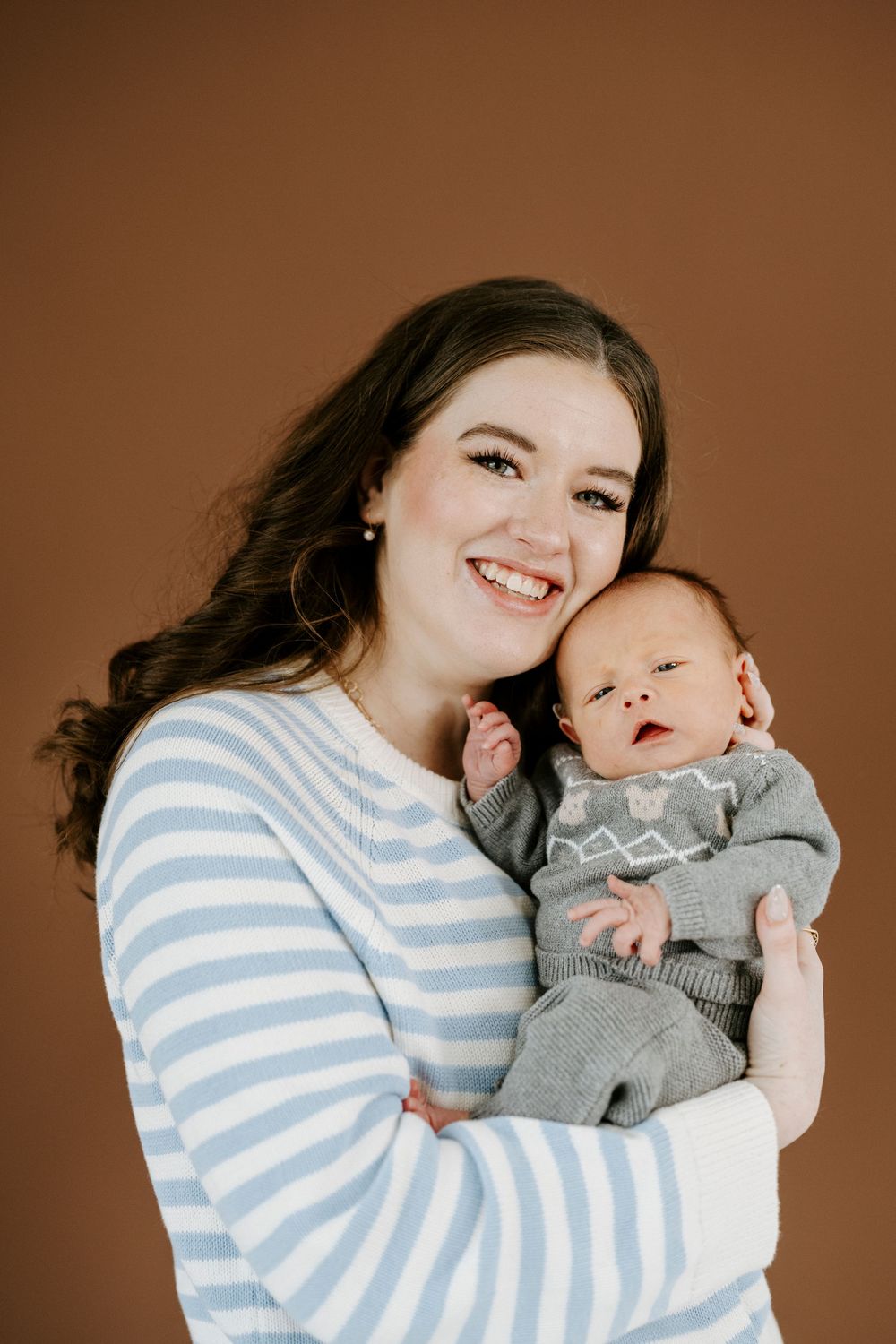 A tender series of portraits showing a parent in a striped sweater holding and embracing a baby in gray against a brown backdrop.