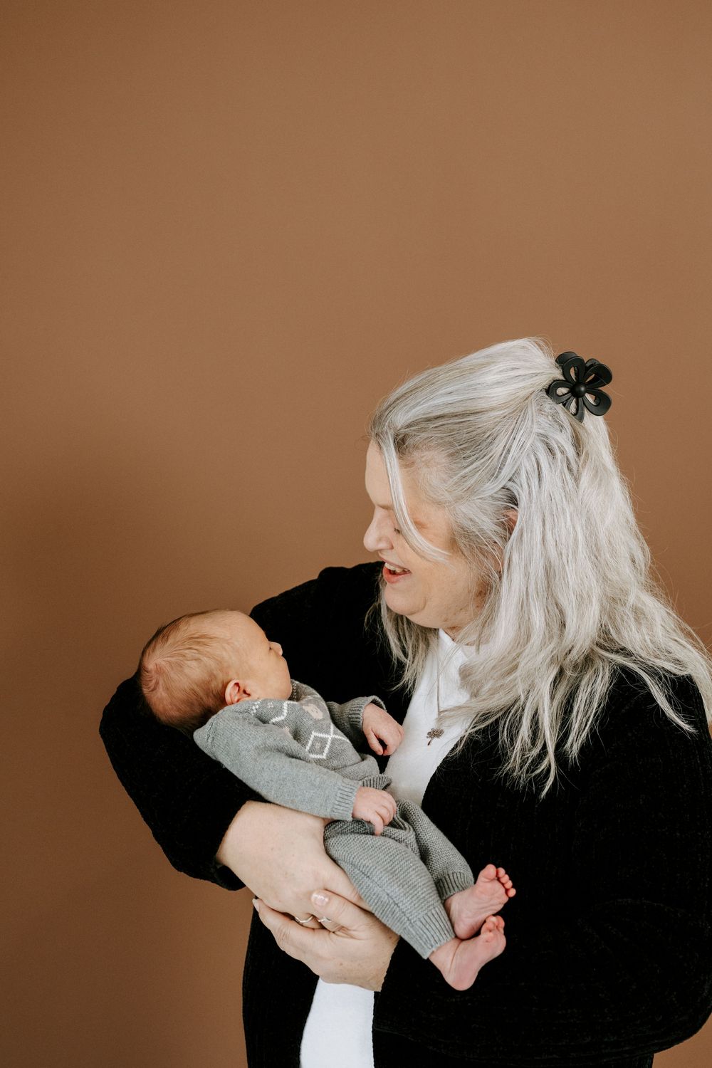 Intimate portrait series of someone in black clothing holding and bonding with a baby in light clothing against warm brown background.