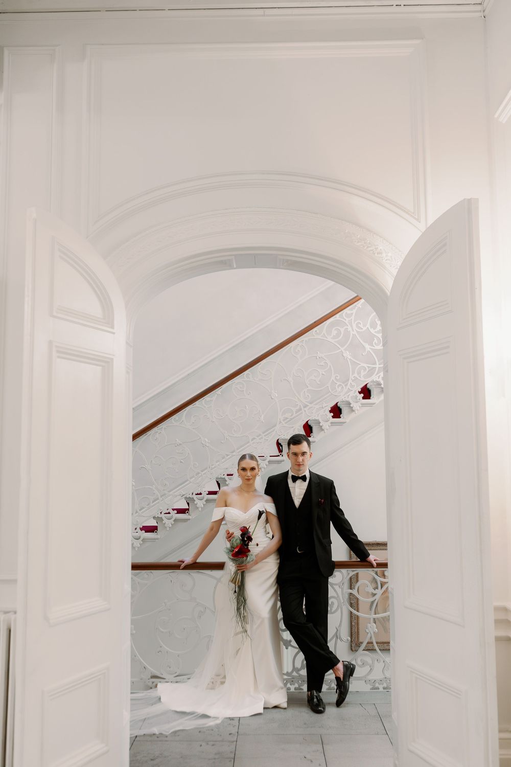 Elegant couple walking through a white arched hallway decorated with hanging lights for their wedding.