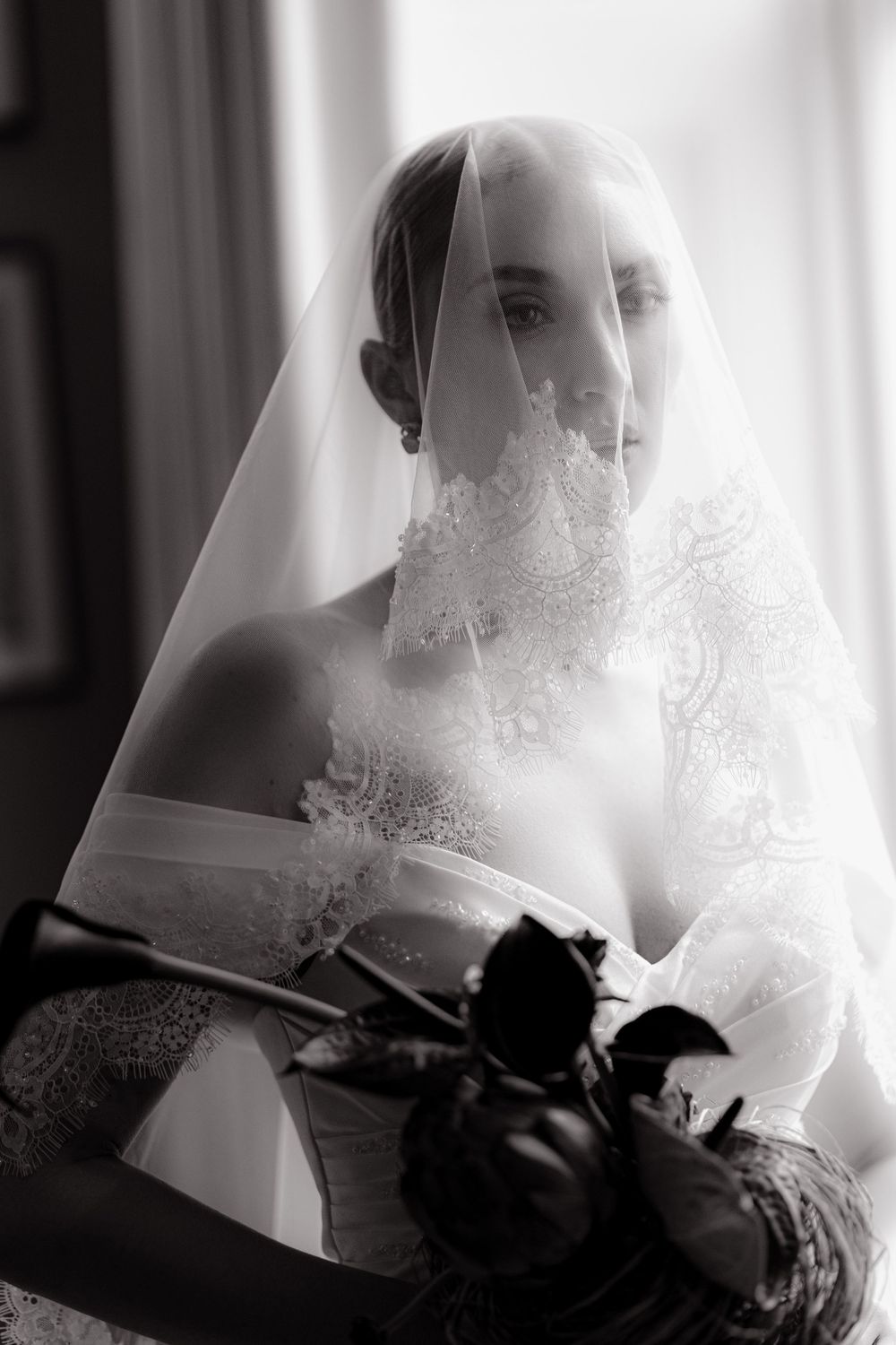 A dramatic black and white bridal portrait with a delicate lace veil and dark roses creating an elegant composition.