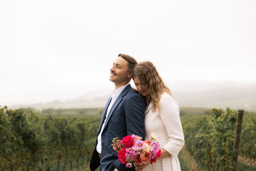 A couple in wedding attire embraces while standing in a misty field during golden hour.