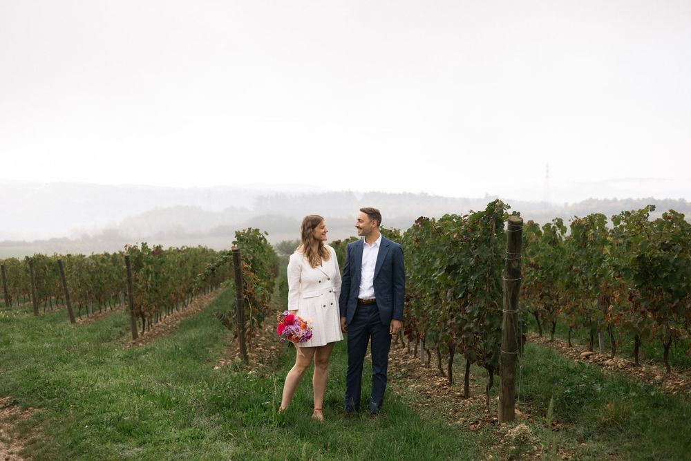 A couple walks through a scenic vineyard on a misty day with rolling hills in the background.