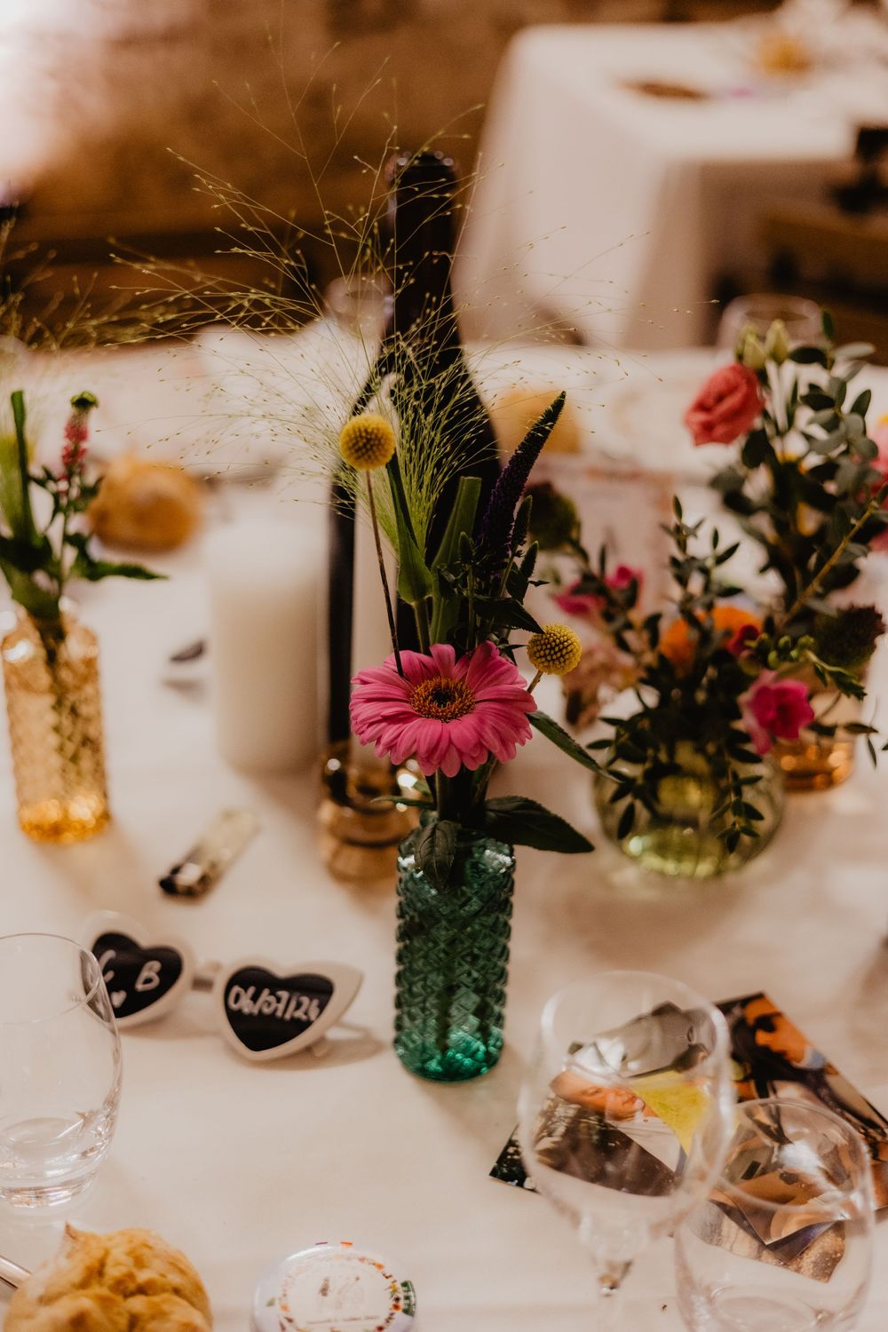 Wedding table decorations with colorful flowers in mason jars and place settings.