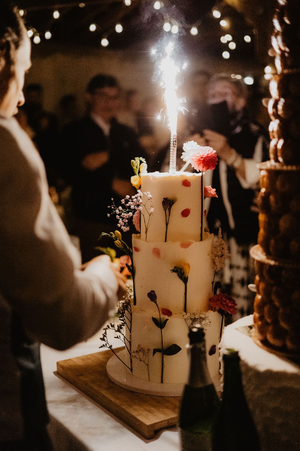 White wedding cake with delicate floral decorations and candles glowing in a dark reception setting.